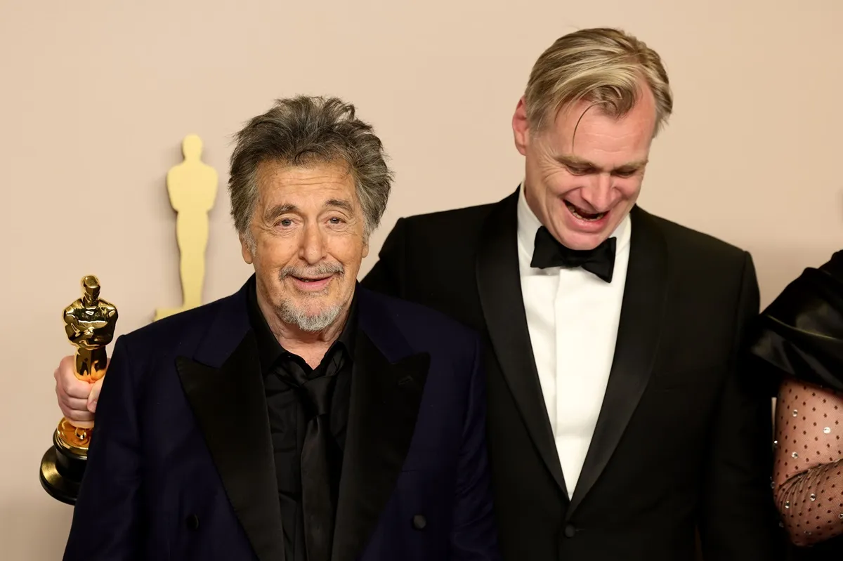 Christopher Nolan posing in a suit next to Al Pacino who's wearing a black suit at the Oscars.