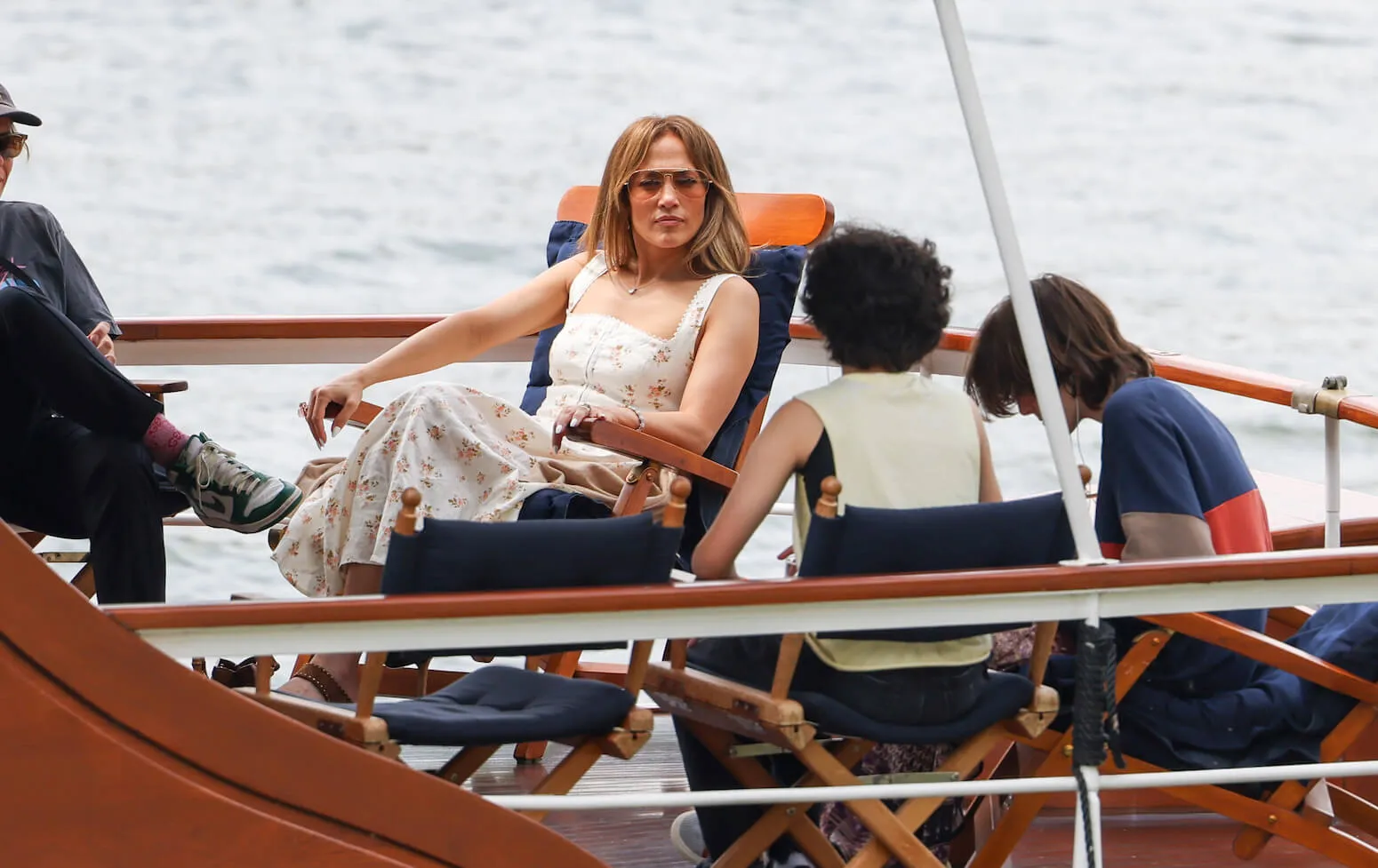 Jennifer Lopez sits in a chair facing her child, Emme Muniz, and Ben Affleck's child, Fin Affleck, while on a boat in Paris.