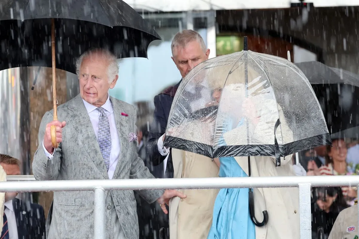 King Charles III and Queen Camilla watch The King’s Parade under torrential rain during visit to Jersey